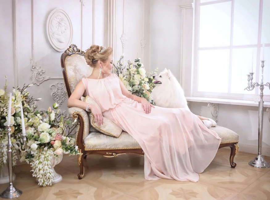 A woman in a flowing pink dress lounges elegantly with a Samoyed dog in a sophisticated, floral-adorned interior. - royal dog names