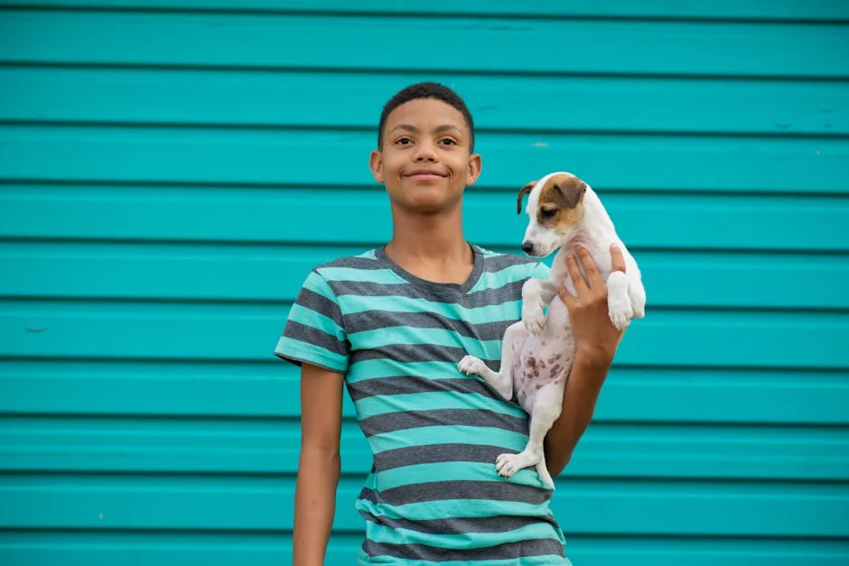 A smiling teenager holds a small puppy against a vibrant teal background. - small dog names boy