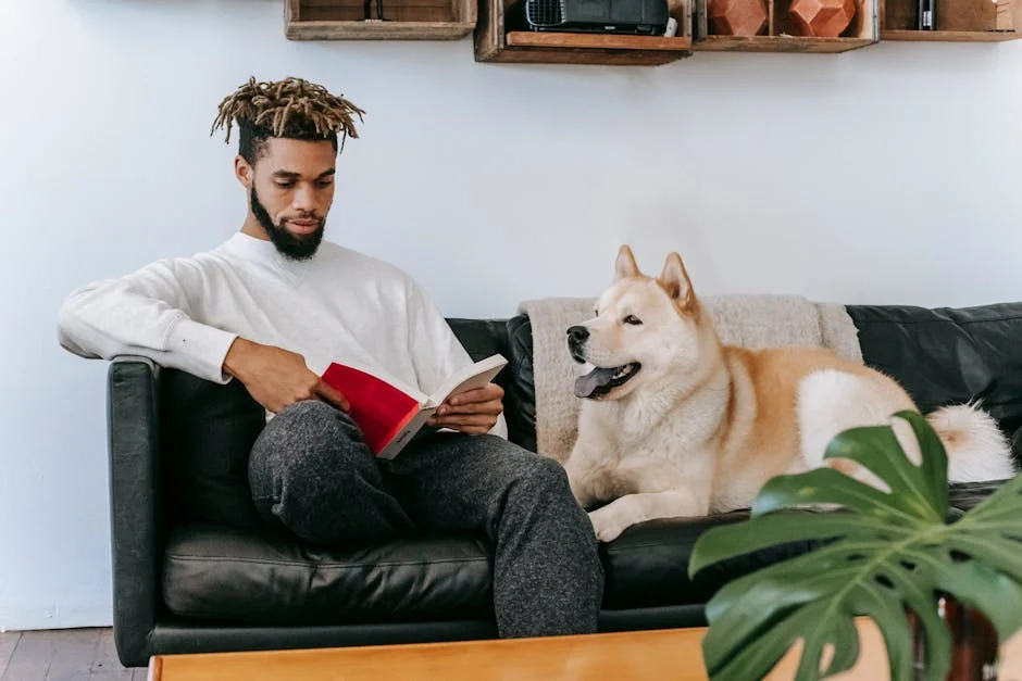 Concentrated African American male sitting on comfortable couch near Akita Inu dog while reading book in living room during weekend - unique male dog names with meaning